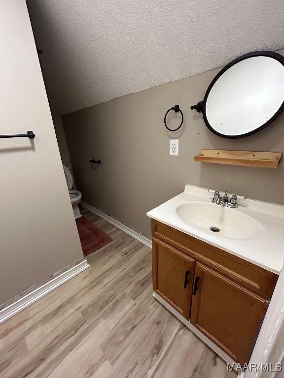 bathroom featuring a textured ceiling, vanity, hardwood / wood-style flooring, toilet, and lofted ceiling