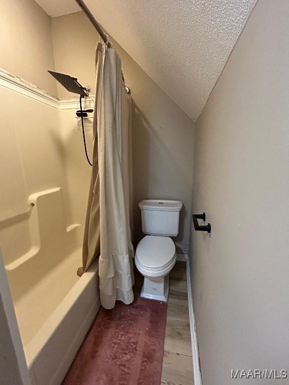 bathroom with vaulted ceiling, toilet, a textured ceiling, shower / tub combo with curtain, and hardwood / wood-style flooring