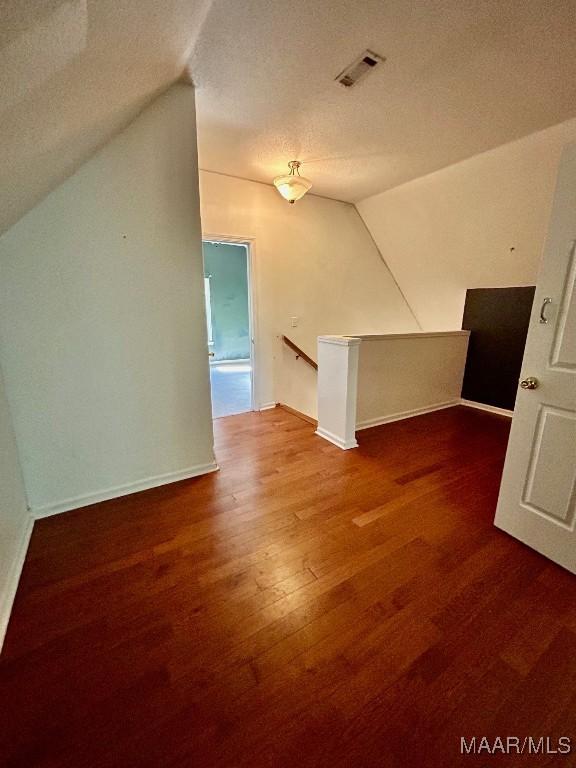 additional living space featuring a textured ceiling, wood-type flooring, and lofted ceiling