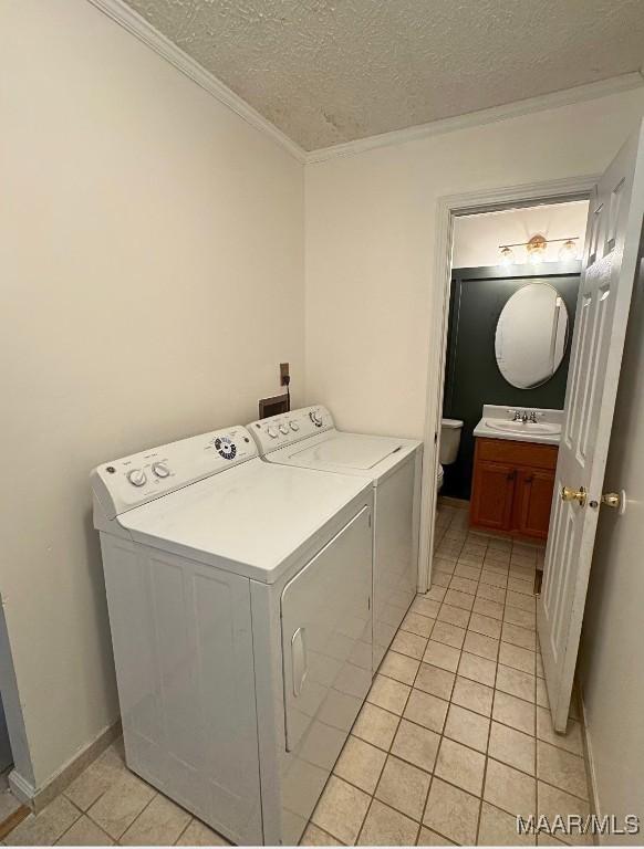 washroom with sink, a textured ceiling, washer and clothes dryer, light tile patterned flooring, and ornamental molding