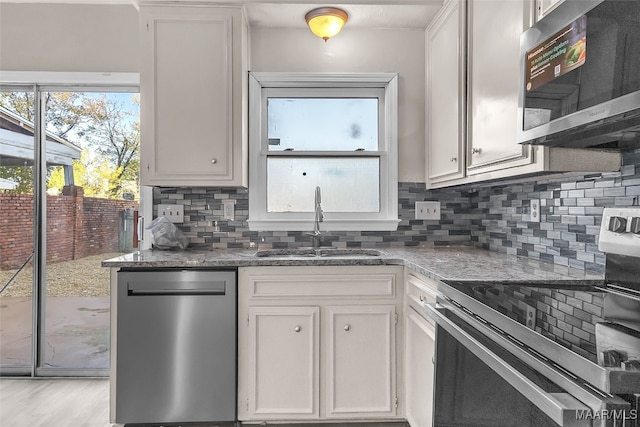 kitchen with appliances with stainless steel finishes, tasteful backsplash, dark stone counters, sink, and white cabinetry