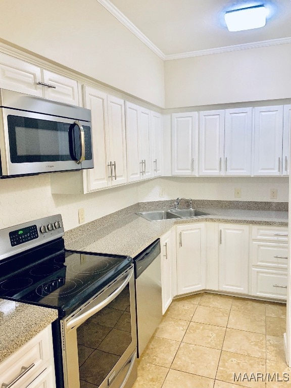 kitchen featuring appliances with stainless steel finishes, ornamental molding, sink, light tile patterned floors, and white cabinetry