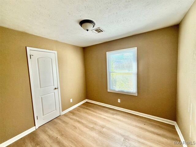 spare room featuring light wood-type flooring and a textured ceiling