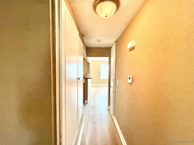 hallway featuring light wood-type flooring and a textured ceiling