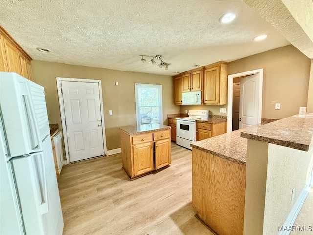 kitchen with light brown cabinets, white appliances, light hardwood / wood-style flooring, a textured ceiling, and a kitchen island