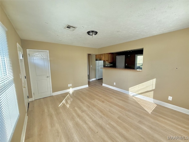 unfurnished living room featuring a healthy amount of sunlight, a textured ceiling, and light hardwood / wood-style flooring