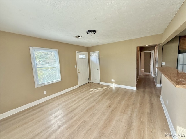 unfurnished room with light wood-type flooring and a textured ceiling