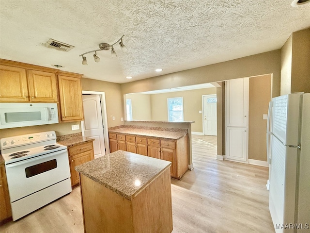 kitchen featuring a kitchen island, light wood-type flooring, white appliances, and a textured ceiling