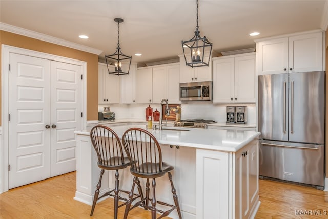 kitchen with appliances with stainless steel finishes, light wood-type flooring, white cabinetry, and a kitchen island with sink