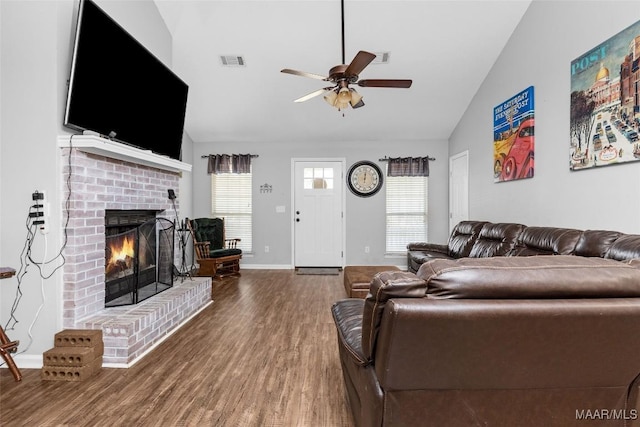 living room with visible vents, a ceiling fan, wood finished floors, vaulted ceiling, and a brick fireplace