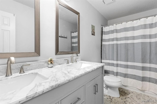 full bathroom with double vanity, a textured ceiling, toilet, and a sink