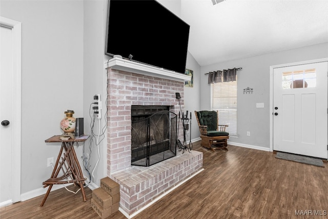 living area featuring a brick fireplace, vaulted ceiling, baseboards, and wood finished floors