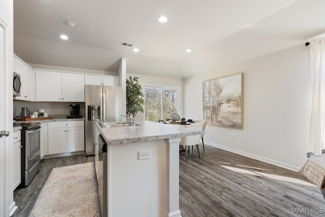 kitchen with lofted ceiling, a kitchen island with sink, white cabinets, wood-type flooring, and stainless steel appliances