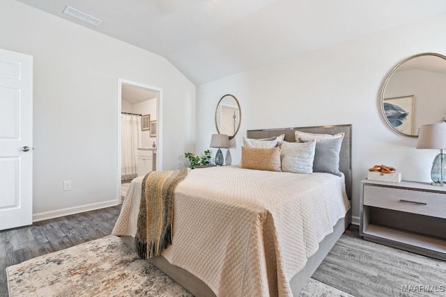 bedroom featuring hardwood / wood-style floors, ensuite bathroom, and lofted ceiling