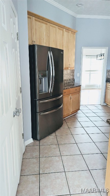 kitchen featuring tasteful backsplash, stainless steel refrigerator with ice dispenser, dark stone countertops, crown molding, and light tile patterned floors