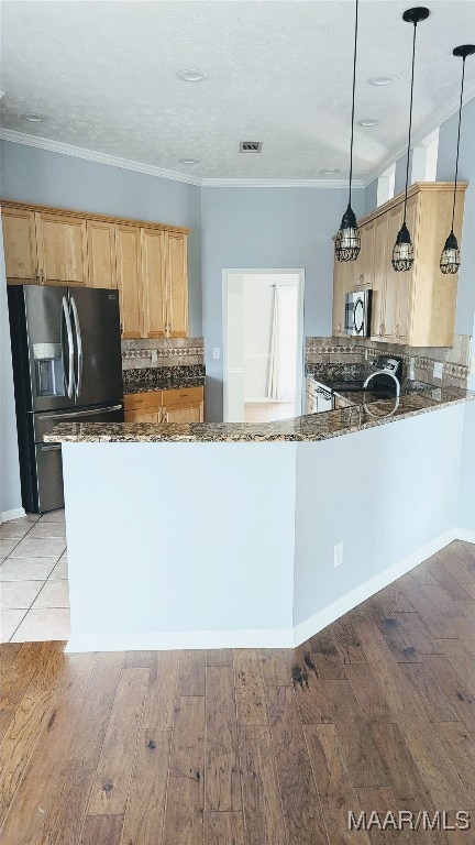 kitchen featuring kitchen peninsula, appliances with stainless steel finishes, dark stone counters, decorative light fixtures, and light hardwood / wood-style floors