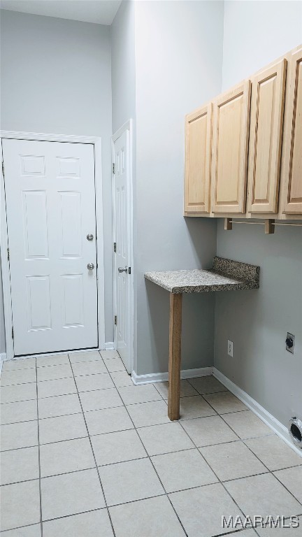 clothes washing area with electric dryer hookup, a towering ceiling, light tile patterned flooring, and cabinets