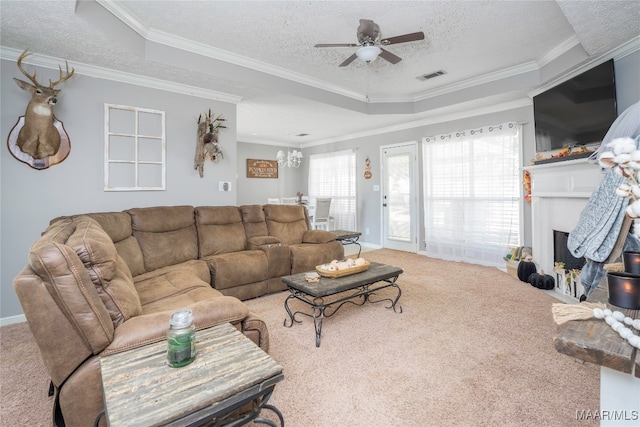 living room featuring carpet flooring, a textured ceiling, a tray ceiling, ceiling fan with notable chandelier, and crown molding