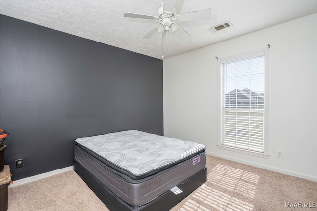 bedroom featuring a textured ceiling, light colored carpet, and ceiling fan