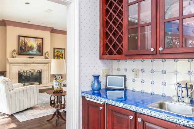 bar featuring ornamental molding, sink, wood-type flooring, tile countertops, and a fireplace