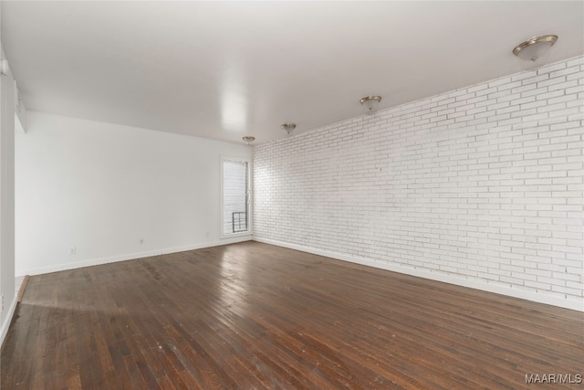 spare room featuring dark hardwood / wood-style floors and brick wall