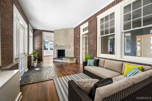 living room featuring a fireplace, dark wood-type flooring, and brick wall