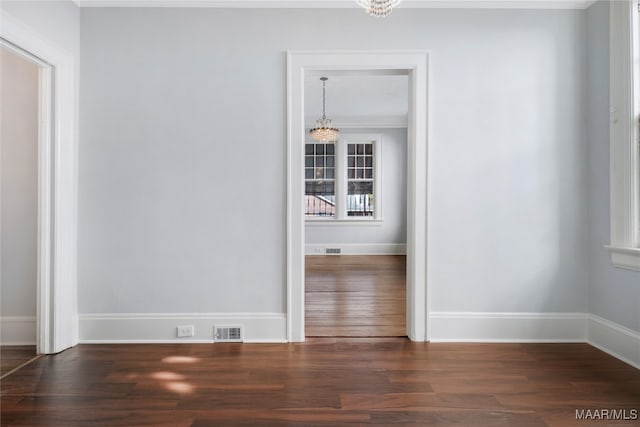 empty room with an inviting chandelier, crown molding, and dark wood-type flooring