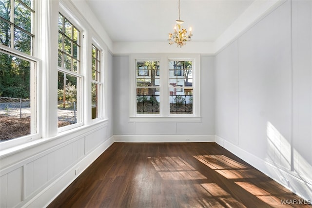 unfurnished dining area featuring a notable chandelier, a healthy amount of sunlight, and dark hardwood / wood-style flooring