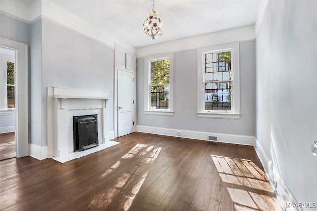 unfurnished living room featuring a textured ceiling, a tiled fireplace, a chandelier, and dark hardwood / wood-style floors