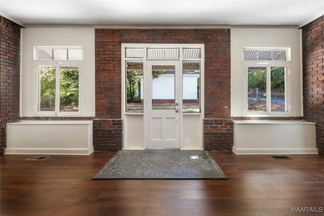 foyer entrance with dark hardwood / wood-style floors, crown molding, and brick wall