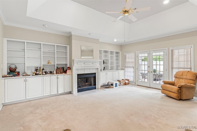 living room featuring a tile fireplace, ceiling fan, french doors, crown molding, and light colored carpet