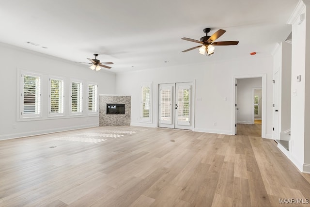 unfurnished living room featuring ornamental molding, light wood-type flooring, a stone fireplace, and a healthy amount of sunlight