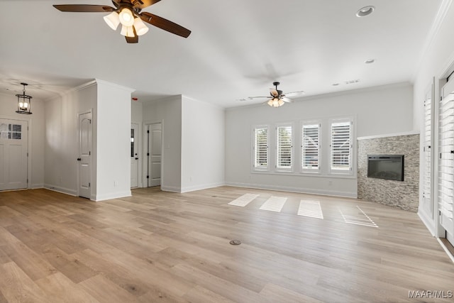 unfurnished living room with ceiling fan with notable chandelier, a stone fireplace, light wood-type flooring, and crown molding