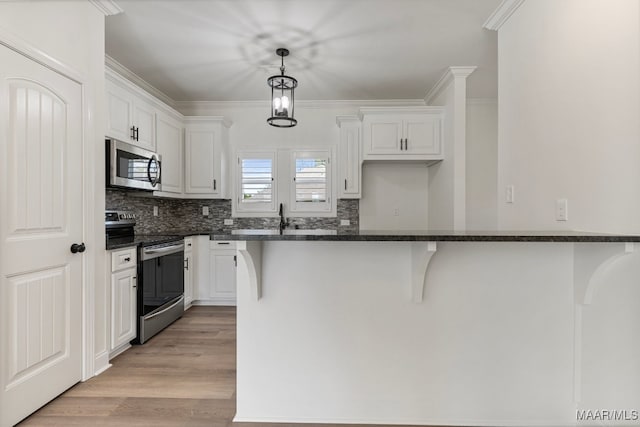 kitchen with appliances with stainless steel finishes, decorative light fixtures, a kitchen bar, white cabinets, and light wood-type flooring