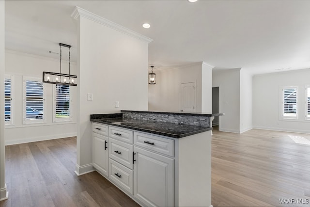 kitchen with kitchen peninsula, ornamental molding, light hardwood / wood-style flooring, white cabinets, and hanging light fixtures