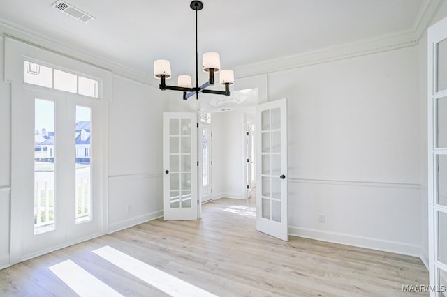 unfurnished dining area with a notable chandelier, ornamental molding, french doors, and light wood-type flooring