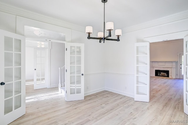 unfurnished dining area featuring ornamental molding, an inviting chandelier, light hardwood / wood-style floors, and french doors