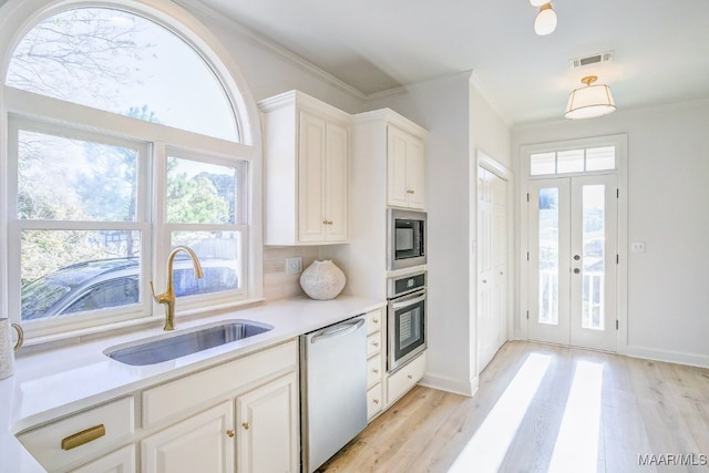 kitchen featuring appliances with stainless steel finishes, sink, white cabinets, decorative backsplash, and light hardwood / wood-style flooring