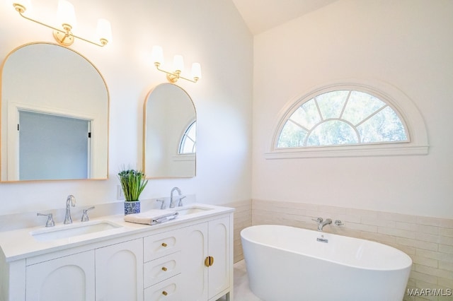 bathroom with tile walls, a tub to relax in, vanity, and plenty of natural light