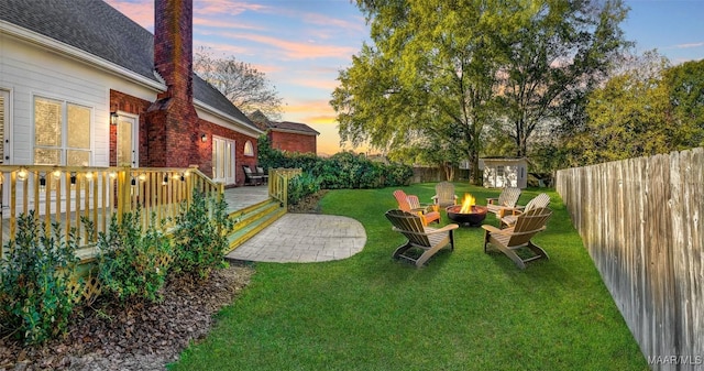 yard at dusk with a wooden deck, an outdoor fire pit, and a storage unit