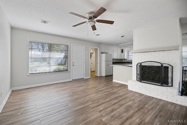 unfurnished living room with hardwood / wood-style flooring, ceiling fan, a fireplace, and a textured ceiling