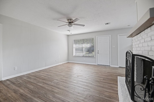 unfurnished living room with a textured ceiling, a brick fireplace, ceiling fan, and dark wood-type flooring