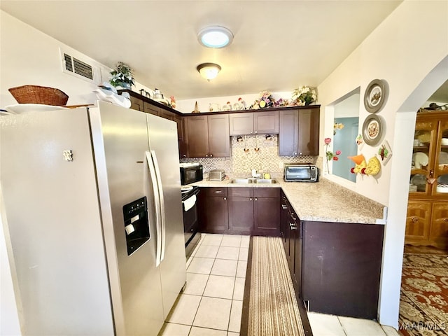 kitchen featuring stainless steel refrigerator with ice dispenser, backsplash, electric range oven, dark brown cabinetry, and light tile patterned flooring