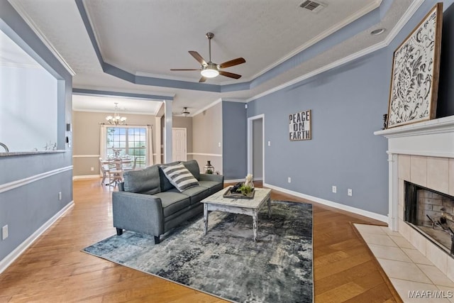 living room with a tile fireplace, light hardwood / wood-style flooring, a raised ceiling, and ornamental molding