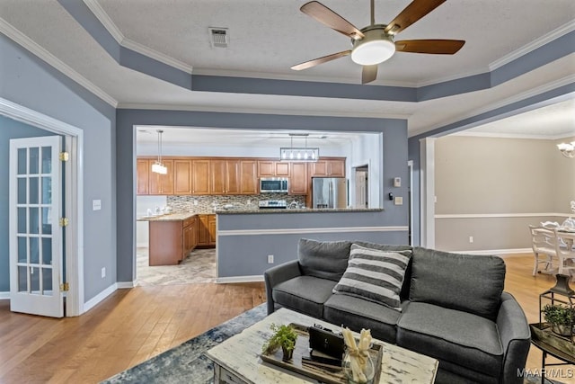 living room featuring ceiling fan with notable chandelier, a raised ceiling, ornamental molding, a textured ceiling, and light hardwood / wood-style floors