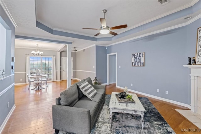 living room featuring wood-type flooring, ceiling fan with notable chandelier, a tray ceiling, and ornamental molding