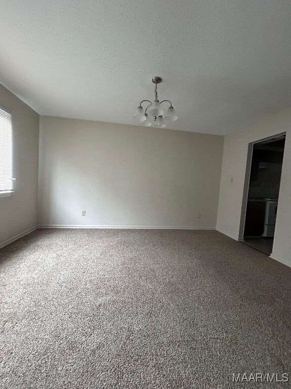 carpeted empty room with a textured ceiling and an inviting chandelier