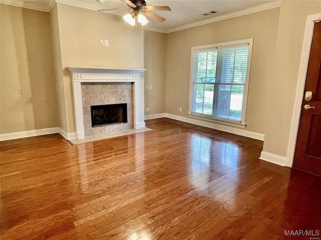 unfurnished living room with a tiled fireplace, crown molding, hardwood / wood-style floors, and ceiling fan