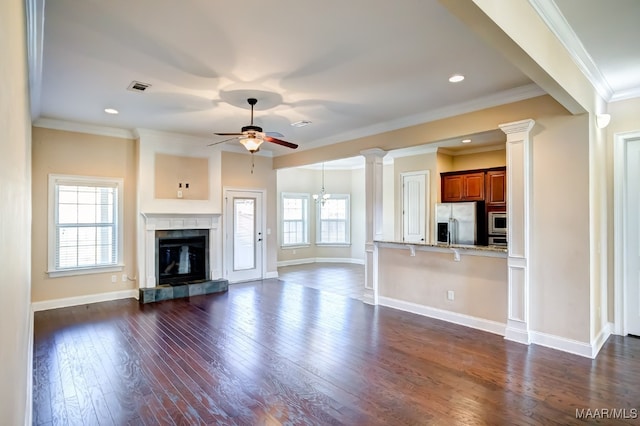 unfurnished living room with a tiled fireplace, crown molding, dark wood-type flooring, and ceiling fan with notable chandelier