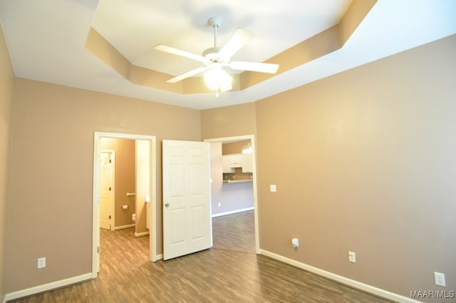 unfurnished bedroom with hardwood / wood-style flooring, ceiling fan, and a tray ceiling